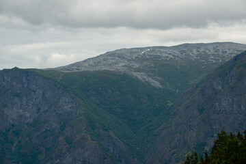 Nature view of Norwegian mountains with white snow cover on its high ground from stegastein viewpoint on a cloudy summer day. Blue uv radiation on the mountains.
