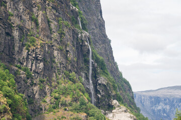 Norwegian fjord mountain scenery with rocks from which a waterfall flows on green plants and trees.