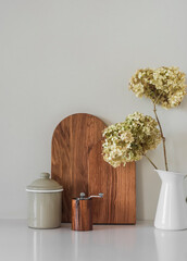 Minimalistic style kitchen interior - cutting boards, a jug of dry hydrangeas on a white table