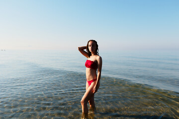 Young bikini model at the beach in red swimsuit. Summer holiday at the seaside where you can swim...
