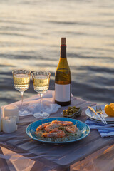 Fototapeta na wymiar Romantic sunset dinner on the beach. Table honeymoon set for two with luxurious food, glasses of champagne drinks in a restaurant with sea view. Summer love, romance date on vacation concept.