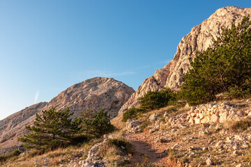 Coastal hiking trail along steep cliffs and mountains near Baska, Krk Otok, Primorje-Gorski Kotar, Croatia, Europe. Deserted barren karst landscape. Tranquil serene atmosphere in summer. Rock climbing