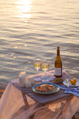 Fototapeta na wymiar Romantic sunset dinner on the beach. Table honeymoon set for two with luxurious food, glasses of champagne drinks in a restaurant with sea view. Summer love, romance date on vacation concept.