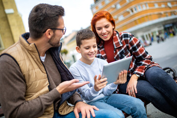 Family sitting on bench, relaxing using gadget, browsing internet.