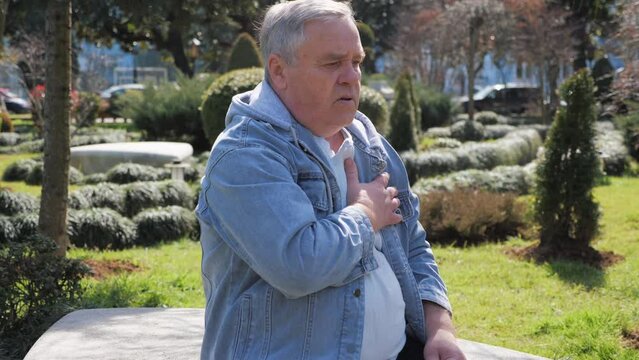 Worried elderly man experiencing chest pain while clutching his heart in park setting.