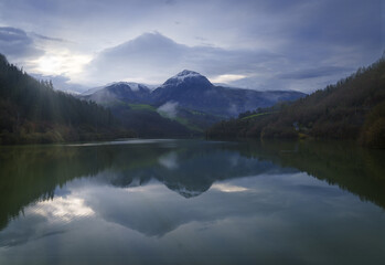 Fototapeta na wymiar Txindoki with snow. Mount Txindoki reflected in the Ibiur reservoir, Basque Country.