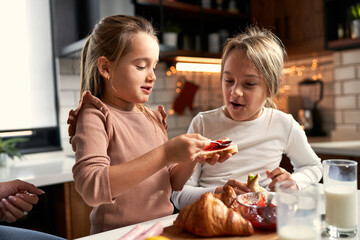  Sweet morning ritual: Mother and daughters joyfully spreading jam on bread, savoring the simple...