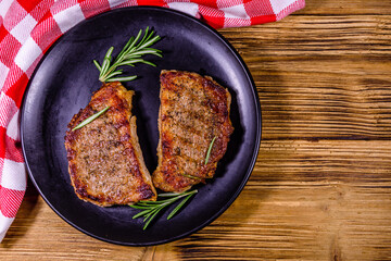 Plate with roasted steaks and rosemary twigs on a wooden table. Top view