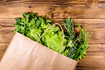 Paper bag with lettuce rosemary and parsley on a wooden table. Vegan food. Top view