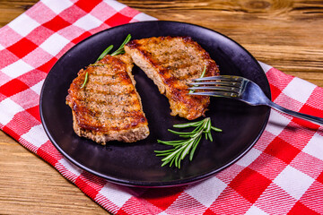 Plate with roasted steaks and rosemary twigs on a wooden table