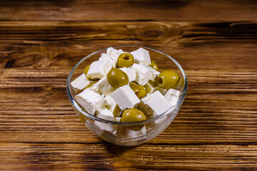 Chopped feta cheese and olives in glass bowl on a wooden table