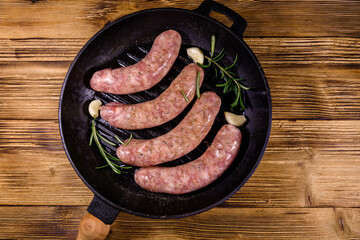 Raw sausages with rosemary twigs and garlic in a cast iron grill pan. Top view