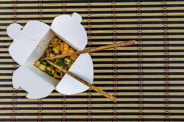 Paper box with pad thai and chopsticks on a bamboo mat. Top view