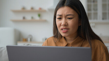 Angry upset Asian japanese woman girl homeowner using laptop in kitchen has problem stressed about...