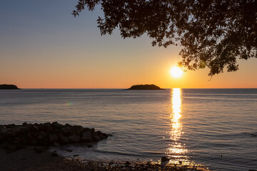 Watching dramatic sunset at coastal village Funtana, Istria, Croatia, EU. Silhouette of remote tropical island. Calm sea surface reflects vibrant colors of sky. Vacation at Adriatic Mediterranean Sea