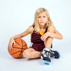 Naklejka premium Little blond basketball player boy sitting on floor with an upset or angry expression while holding his ball