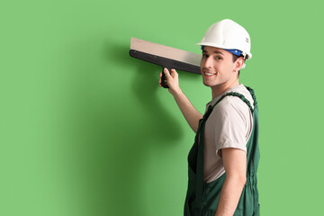 Male worker with putty knife on green background