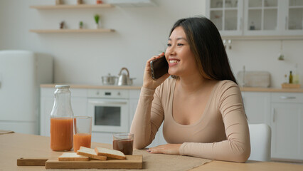 Asian woman talk mobile phone in home kitchen multiethnic chinese japanese girl chatting with...