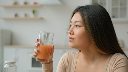 Korean woman drinking fresh smoothie orange juice. Asian vegetarian girl tasting glass of vitamin...