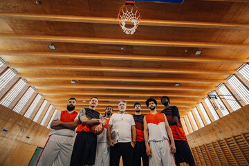 Bottom view of an interracial basketball team with his coach at the hoop.