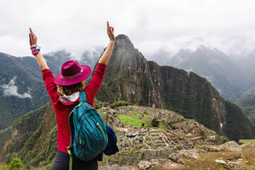 Happy female tourist in a hat with raised hands against the background of Machu Picchu. Cusco. Peru