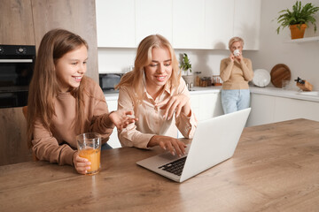 Little girl with her mom using laptop in kitchen