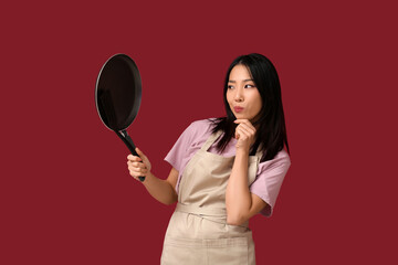 Portrait of thoughtful Asian woman with frying pan on red background