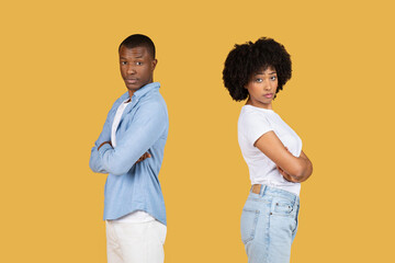 A young man and woman in casual clothing stand back to back with arms crossed