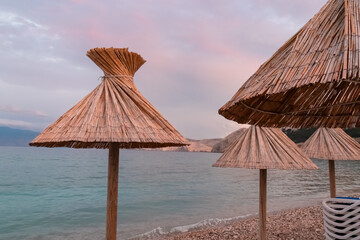 Straw umbrellas at sunrise on idyllic pebble beach in tourist resort town Baska, Krk Otok, Primorje-Gorski Kotar, Croatia, Europe. Paradise summer atmosphere in Kvarner bay, Mediterranean Adriatic Sea