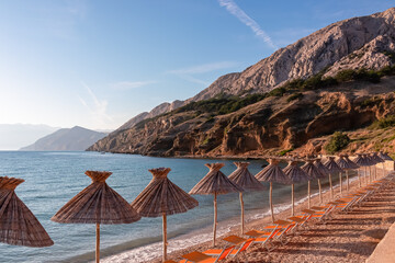 Straw umbrellas and loungers on idyllic pebble beach in resort town Baska, Krk Otok,...