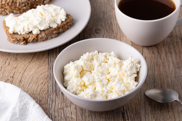 Cottage cheese in a bowl, sandwiches and coffee on a wooden table