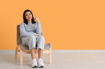 Beautiful young happy woman sitting on comfortable chair near yellow wall