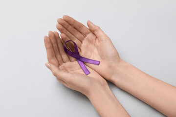 Female hands with purple ribbon on grey background. Cancer concept