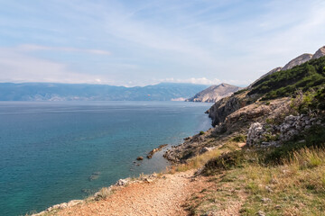 Fototapeta na wymiar Idyllic hiking trail along rugged cliffs in coastal town Baska, Krk Island, Primorje-Gorski Kotar, Croatia, Europe. Vacation in turquoise water bay. Majestic coastline of Mediterranean Adriatic Sea