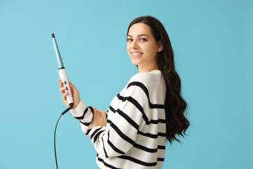 Beautiful young woman with curling iron on blue background