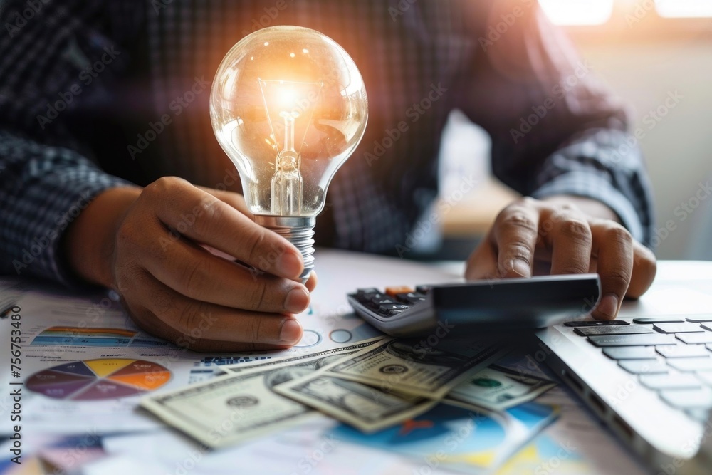 Poster a person sitting at a table with a calculator and a light bulb, ideal for finance or innovation conc