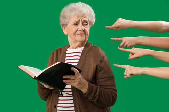 People pointing at senior woman with Holy Bible on green background. Accusation concept - Powered by Adobe