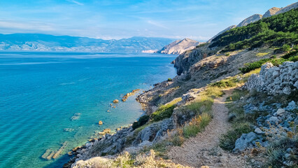 Idyllic hiking trail along rugged cliffs in coastal town Baska, Krk Island, Primorje-Gorski Kotar, Croatia, Europe. Vacation in turquoise water bay. Majestic coastline of Mediterranean Adriatic Sea