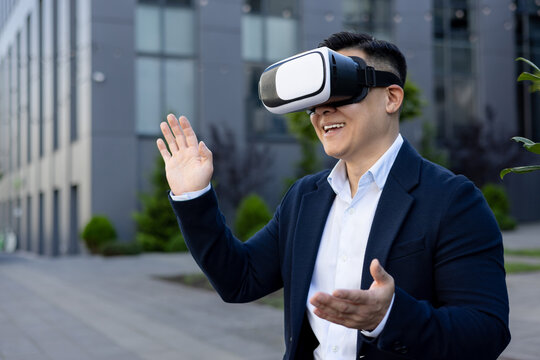 Smiling asian businessman experiencing virtual reality outdoors in modern city setting