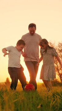 Family team, sports games. Children son daughter play football with father on lawn. Boy girl parent run after red ball in park. Active happy family, child dad having fun playing ball on green grass.