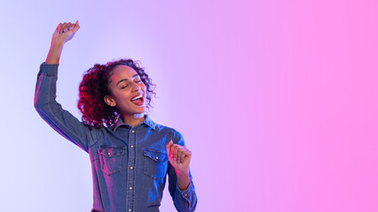 Happy black lady dancing in denim on neon gradient background, free space