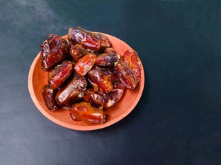 a pile of dates served on a wooden plate on a black background. sweet brown fruit. healthy meals. food for breaking the fast