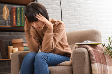 Obraz premium Young woman suffering from headache in armchair at home