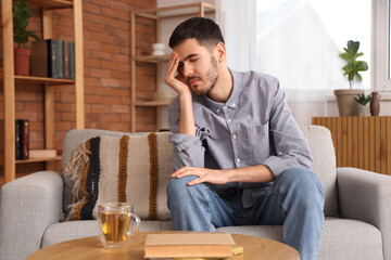 Young man suffering from headache on sofa at home