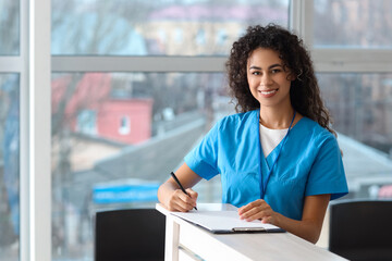 Female African-American medical intern writing in clipboard at hospital
