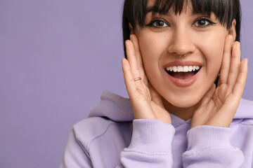 Happy stylish young woman with nose piercing on lilac background