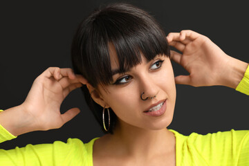 Stylish young woman with nose piercing on black background