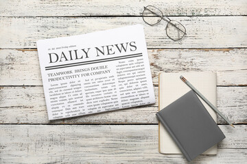 Newspaper with notebook and glasses on white wooden background. Top view