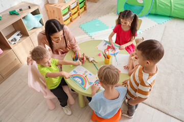 Little children with nursery teacher drawing at table in kindergarten
