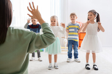 Little children with nursery teacher exercising in kindergarten